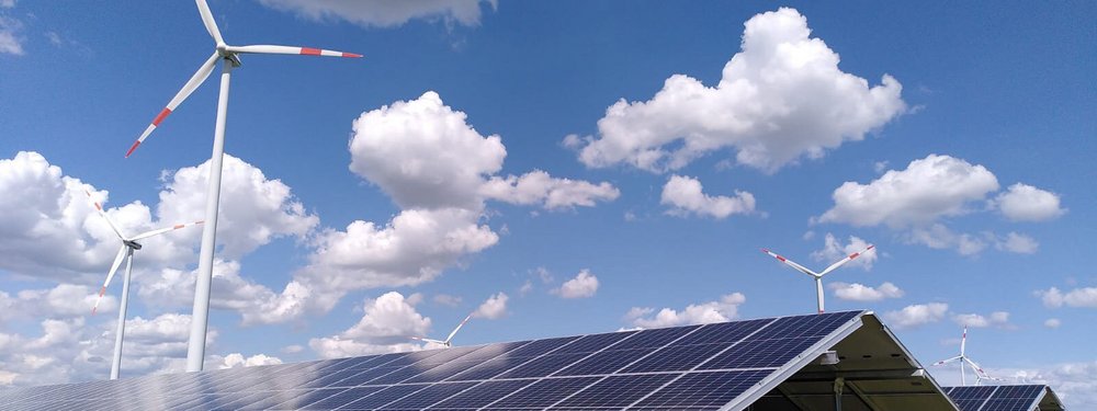 Ansicht des Solarparks Breddin: im Vordergrund stehen PV-Module, im Hintergrund, vor blauem Himmel, stehen Windräder