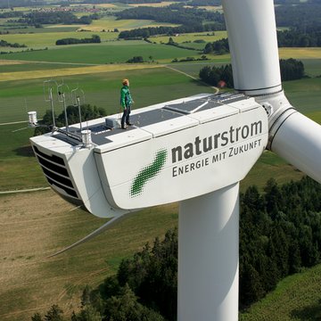 Mensch auf Windkraftanlage mit Schriftzug NATURSTROM